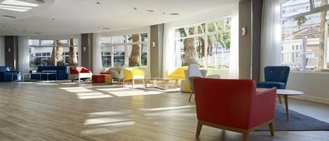 A spacious lobby with a wooden floor, large windows, and modern seating arrangements.