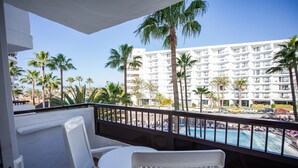 A balcony with white chairs and a small table, overlooking a pool and a white building with balconies. - Servatur Waikiki (San Bartolomé de Tirajana)