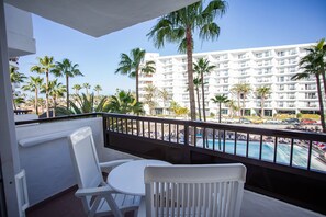 A balcony with white chairs and a small table, overlooking a pool and a white building with balconies. - Servatur Waikiki (San Bartolomé de Tirajana)