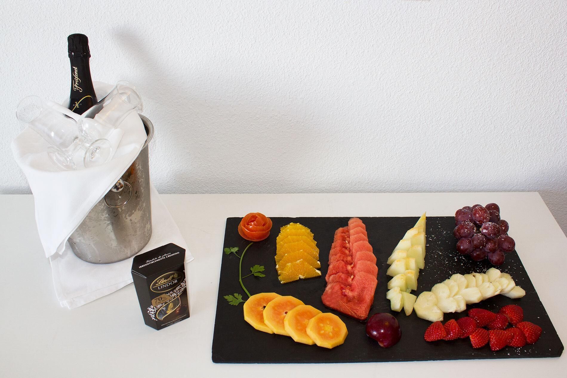 A selection of fruits and a bottle of champagne in a glass container on a table.