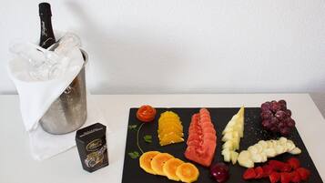 A selection of fruits and a bottle of champagne in a glass container on a table.
