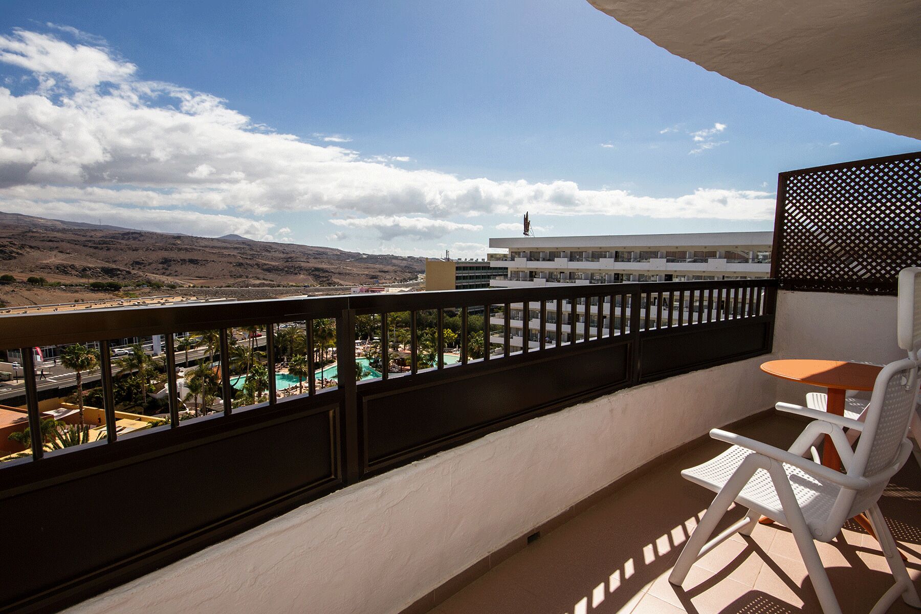 Un balcón con vista a una piscina, un edificio con una bandera y un paisaje montañoso.