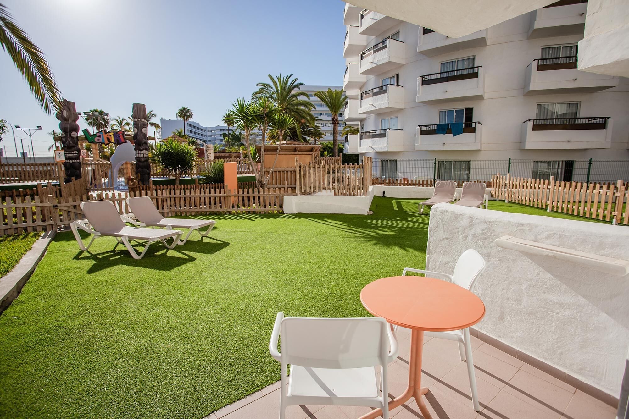 Eine Außenpatio-Terrasse mit Kunstgrasanlage, weißen Lounge-Stühlen und einem kleinen orangefarbenen Tisch.