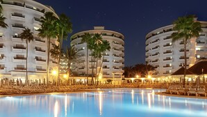 Un hotel con una piscina grande, varios balcones y palmeras.