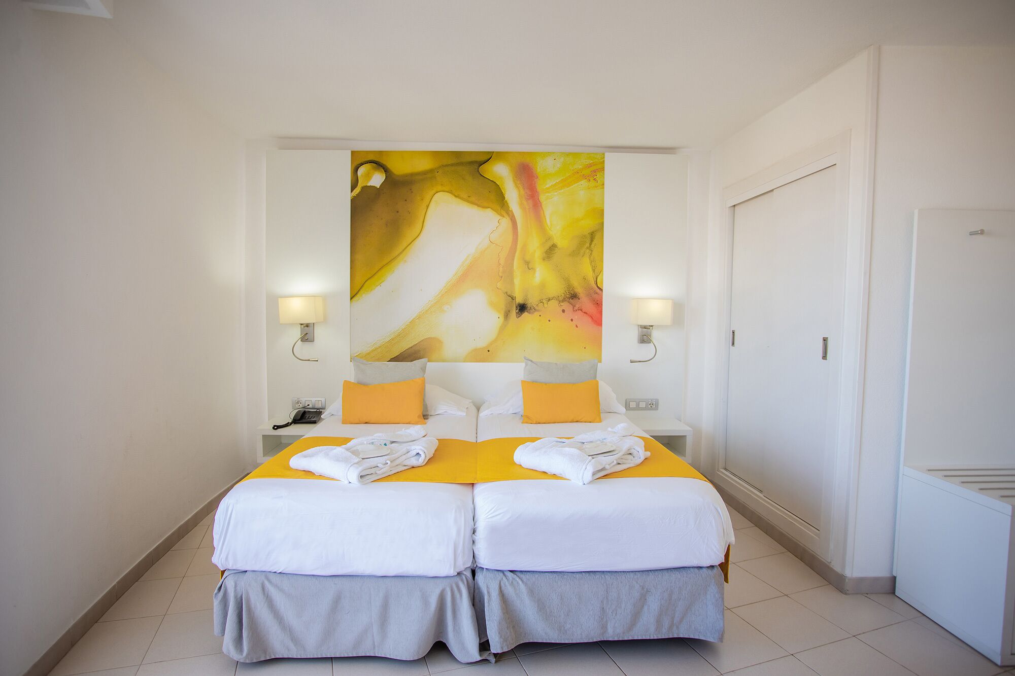 Habitación de hotel con una cama doble, dos lámparas de noche, un cuadro abstracto grande en la pared y una puerta a la derecha.