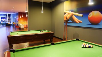 Una mesa de billar con bolas, taco y una mesa de pool en una habitación con pared verde y un cartel de taco y bola.