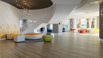 Un vestíbulo espacioso con una escalera moderna, zonas de estar cómodas y grandes ventanales que ofrecen vistas a palmeras.