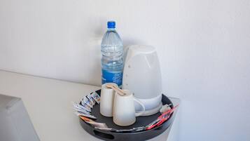 Ett litet bord med en vattenflaska, en vit mugg, en vit kopp och en vit vattenkokare.