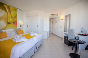 A hotel room with two beds, a desk, a chair, a mirror, and a bathroom door. - Servatur Waikiki (San Bartolomé de Tirajana)