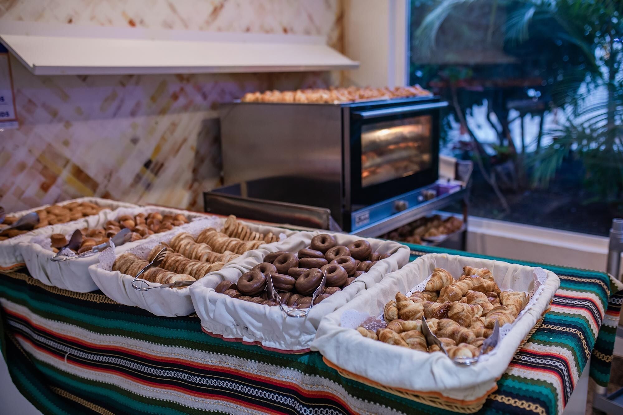Uma mesa de buffet com diversos produtos de pastelaria, incluindo croissants e doces, dispostos em cestas.
