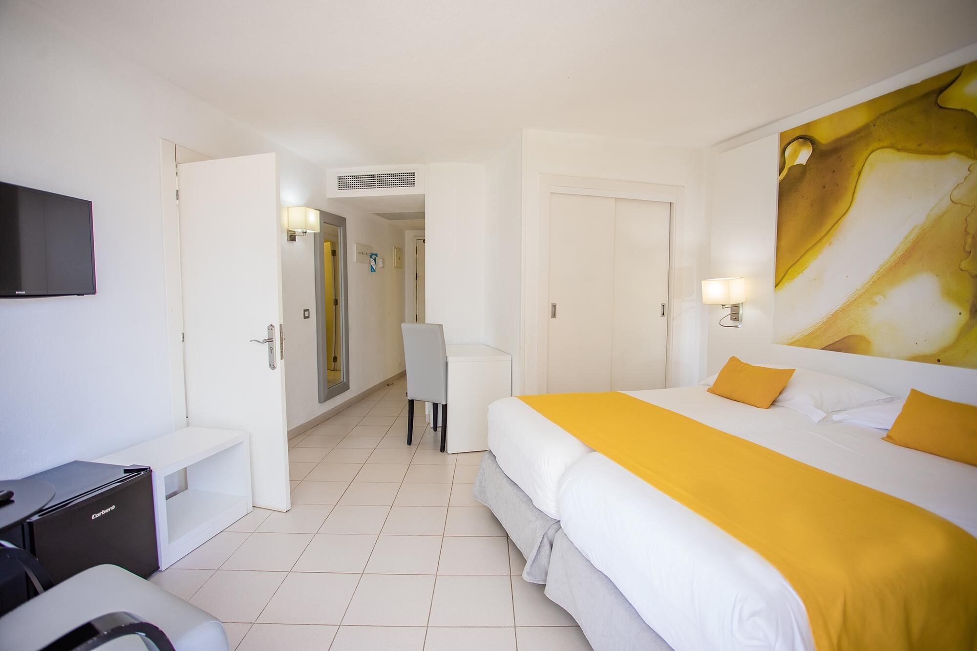 A hotel room with a bed, a desk, a chair, a TV, and a bathroom visible through an open door.