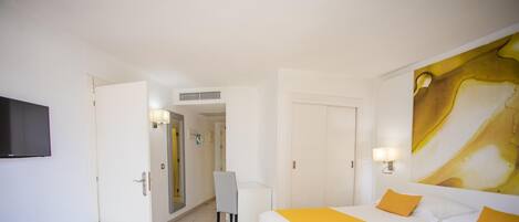 A hotel room with a bed, a desk, a chair, a TV, and a bathroom visible through an open door.