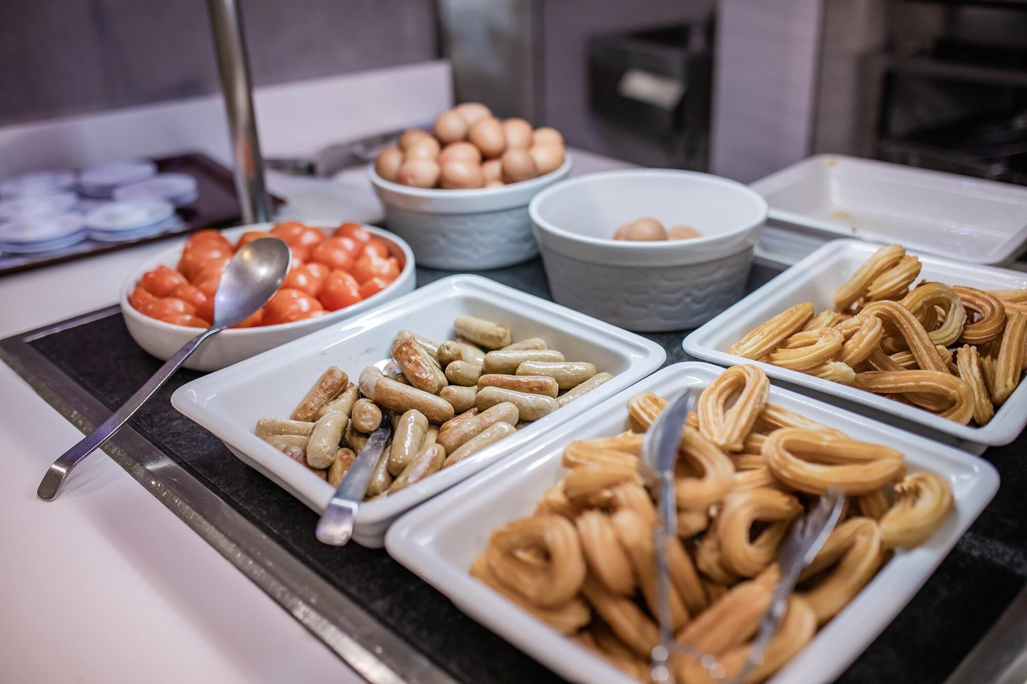 Un bufé con diversas opciones de comida, incluyendo salchichas, pasteles y huevos.