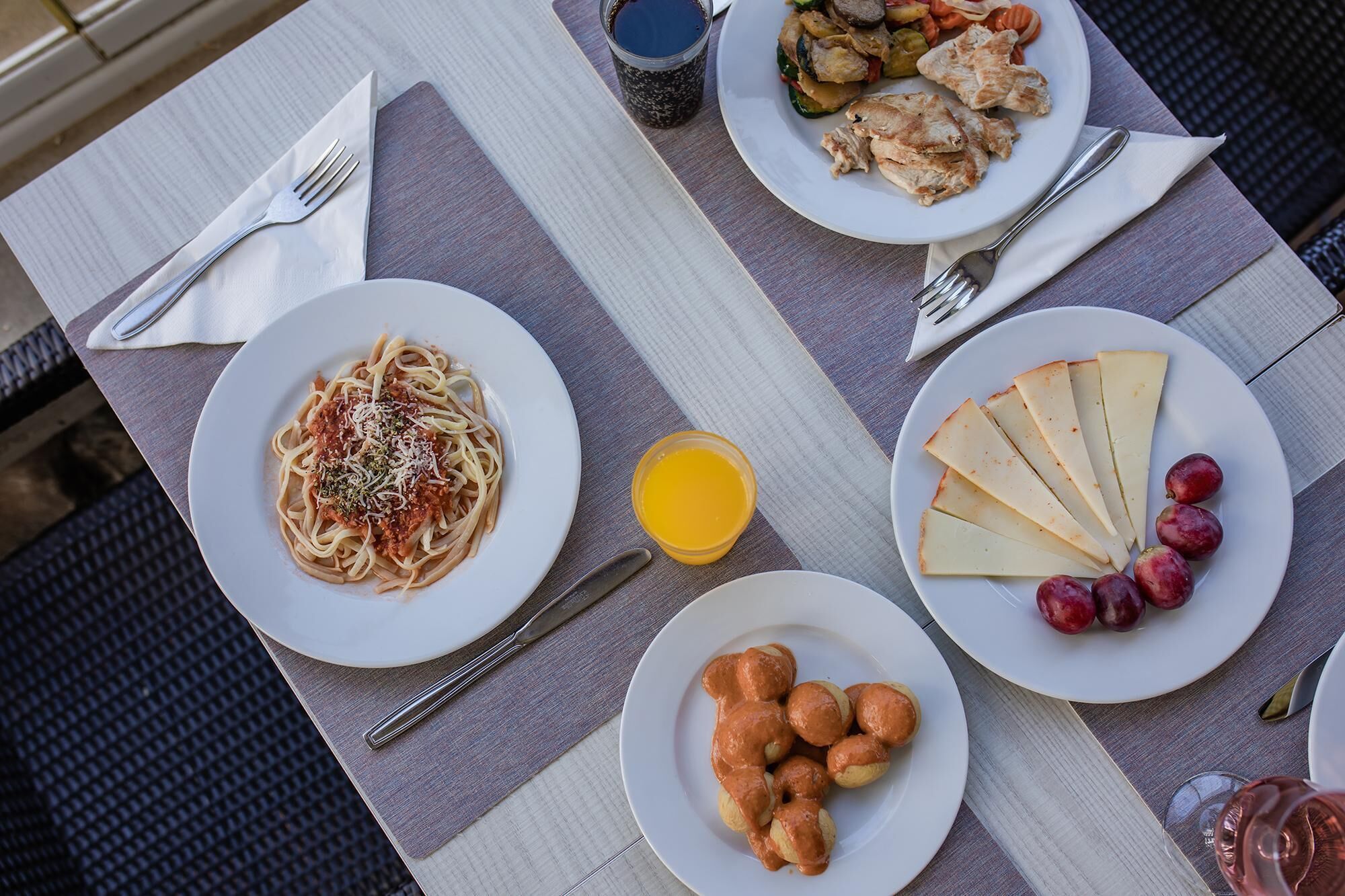 Une table avec des assiettes remplies de nourriture, notamment des pâtes, du fromage et des fruits, ainsi qu'un verre de jus d'orange.