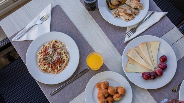 Una mesa con platos de comida que incluyen pasta, queso y fruta, junto con un vaso de jugo de naranja.