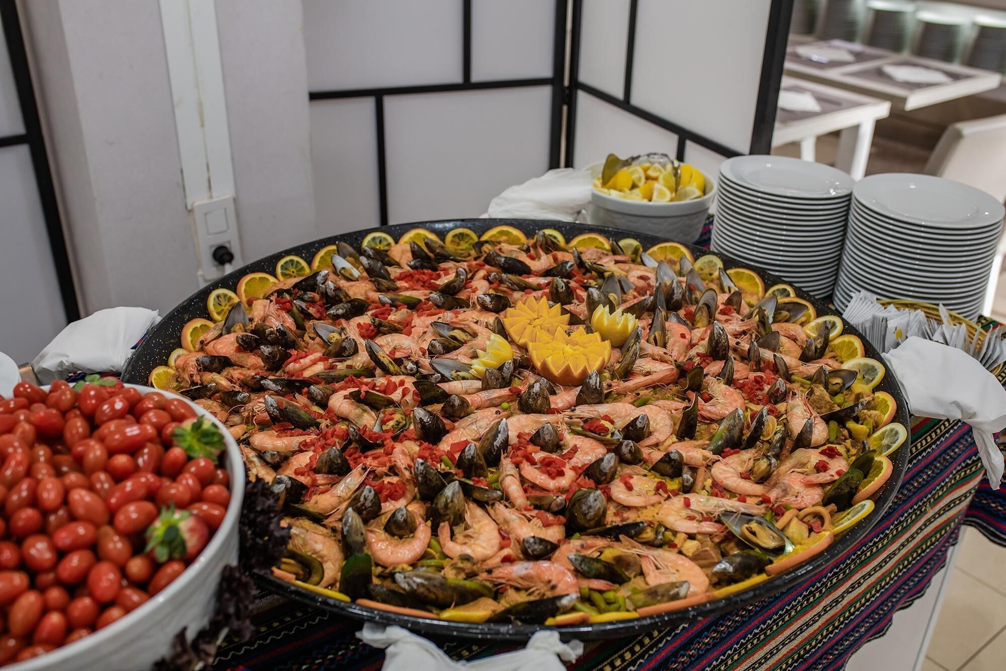 Un plat de marisc amb diversos crustacis i gambes, envoltat de plats i un bol de tomàquets cherry.