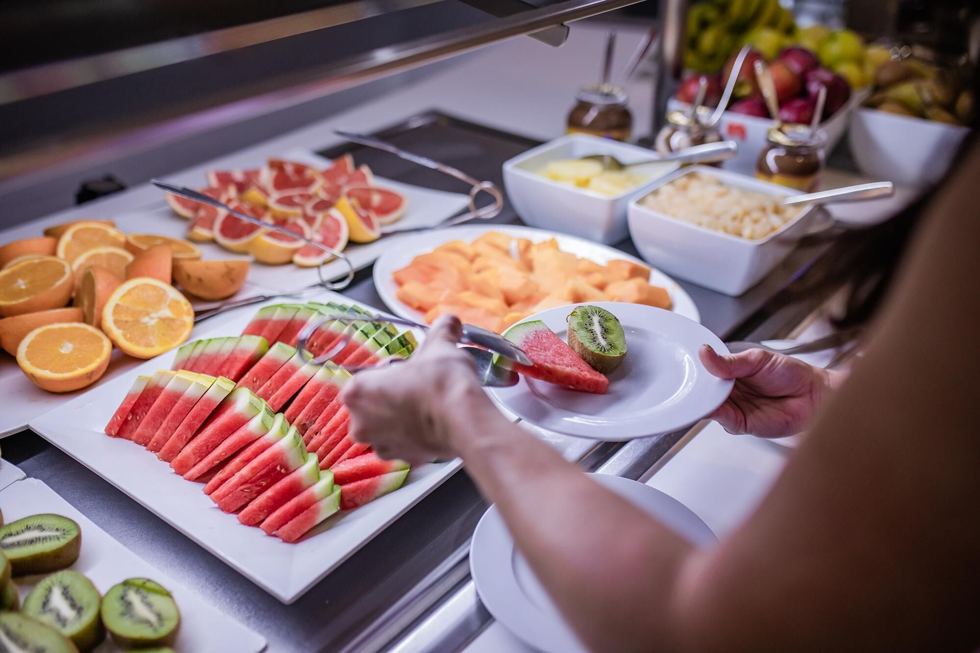 Een buffet met verschillende soorten fruit en een persoon die zich bedient.
