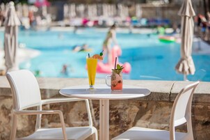 Mesa junto a la piscina con dos bebidas, vista despejada a la piscina y sillas de descanso.