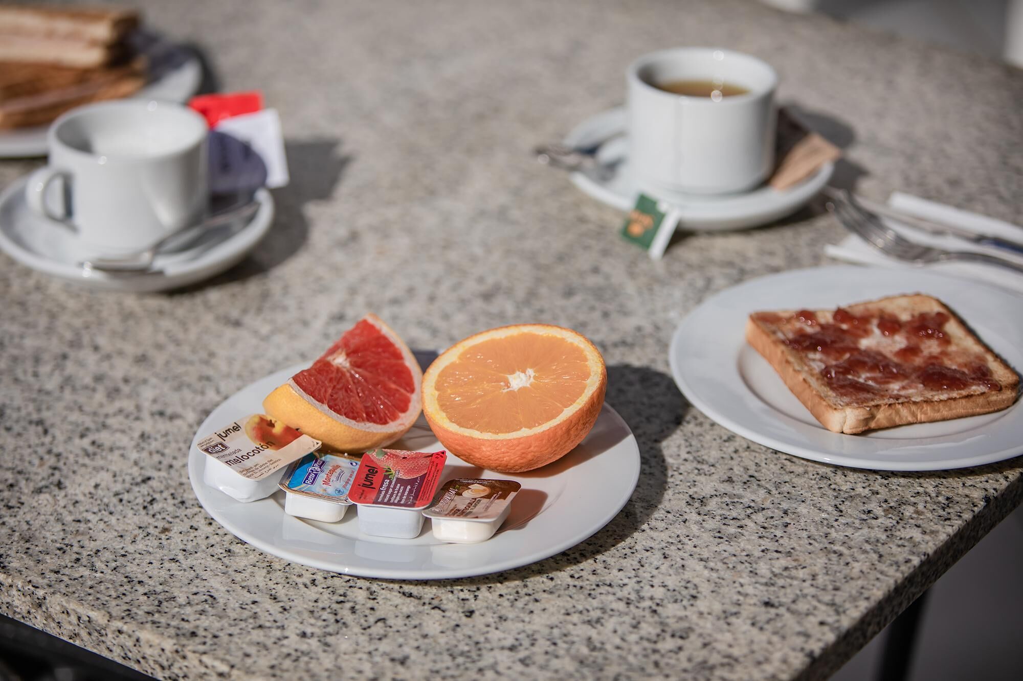 Una colazione servita su un bancone in granito, con pane tostato, pompelmo, arancia e parfait di yogurt.
