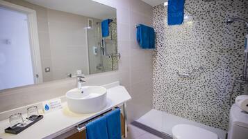 Un baño moderno con un lavabo blanco, un espejo, una ducha con un revestimiento de mosaicos y un inodoro.