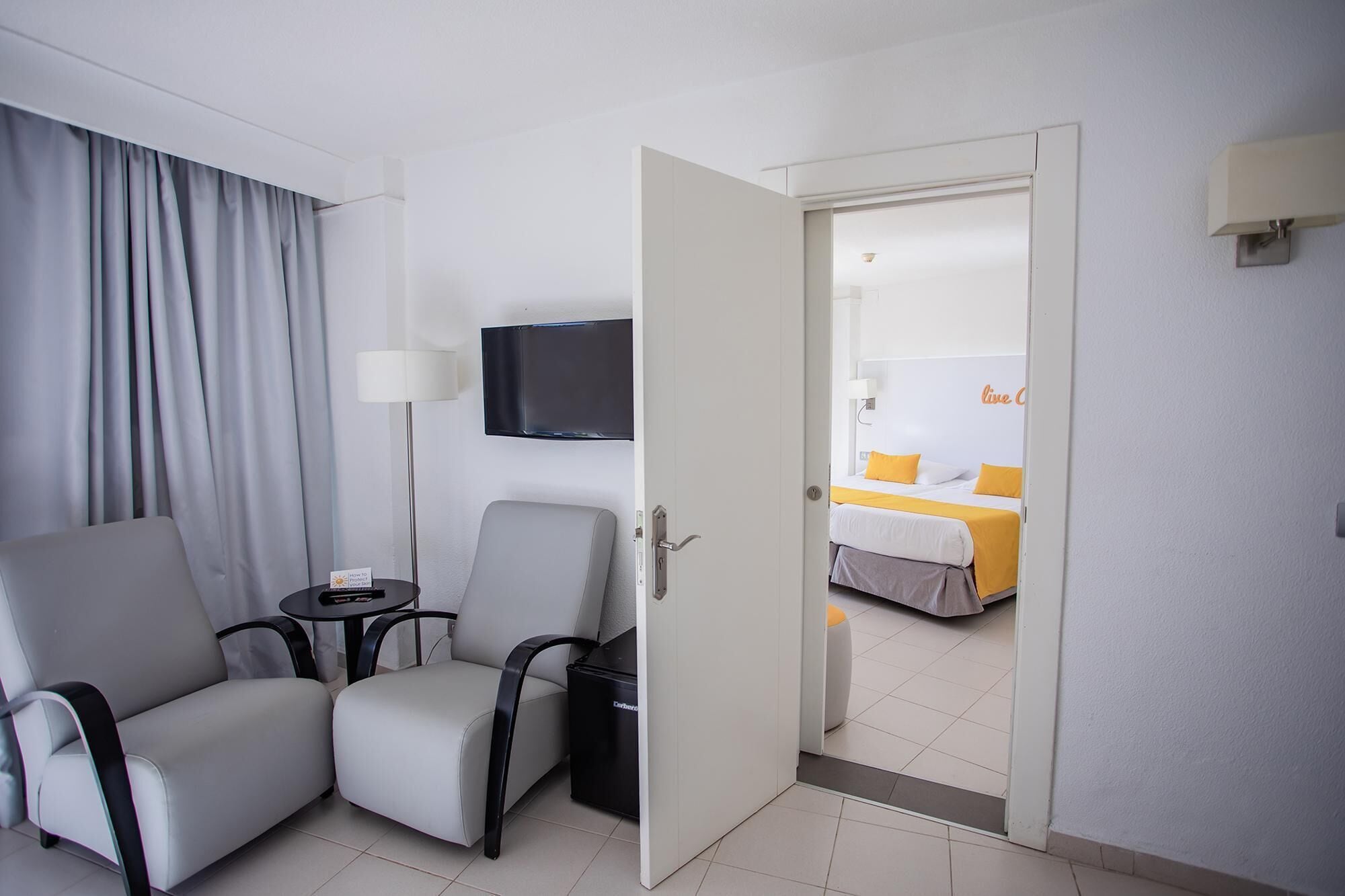 A hotel room with a seating area, a television, and a bed with yellow bedding.