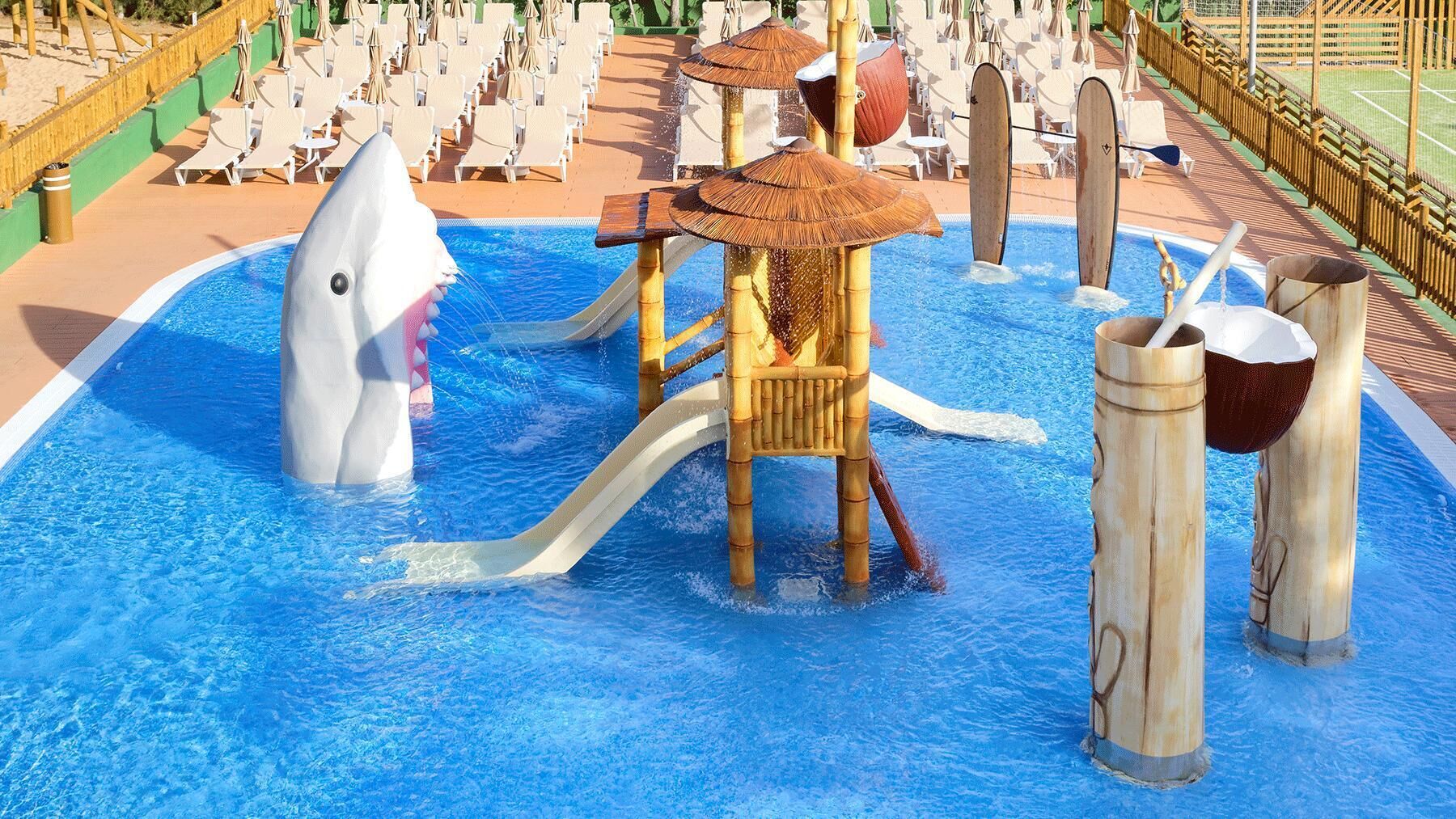 A water park with a shark slide, a play structure, and lounge chairs.