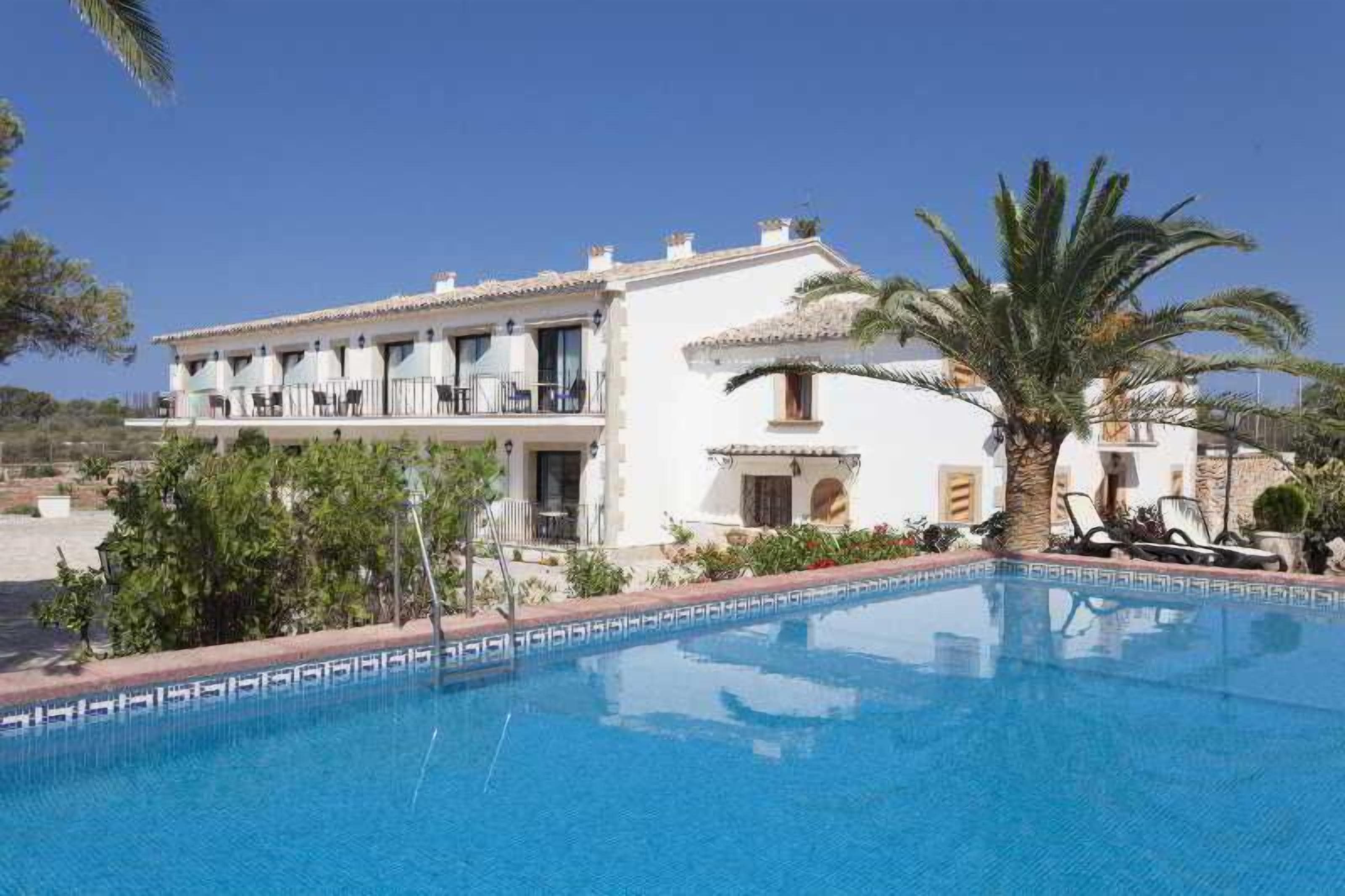 Ein Hotel mit Schwimmbad, ein weißes Gebäude mit Balkonen und eine Palme.