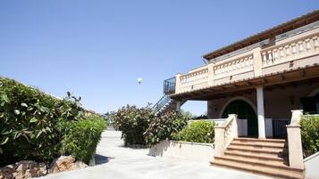A building with a staircase leading to a balcony, surrounded by greenery.