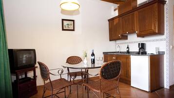 A compact kitchen with a dining area, wooden cabinets, a television, and a small island with a coffee maker.