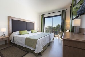 A hotel room with a large bed, two bedside tables, a desk, and a balcony with a view of palm trees. - Sa Bassa Plana (Llucmajor)