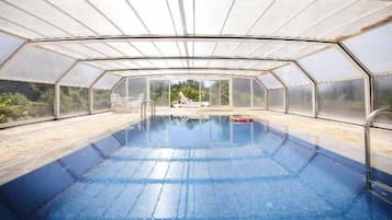 A swimming pool with a glass enclosure, surrounded by a wooden deck and a chair.