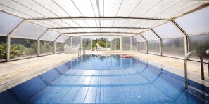 A swimming pool with a glass enclosure, surrounded by a wooden deck and a chair. - Sa Bassa Plana (Llucmajor)