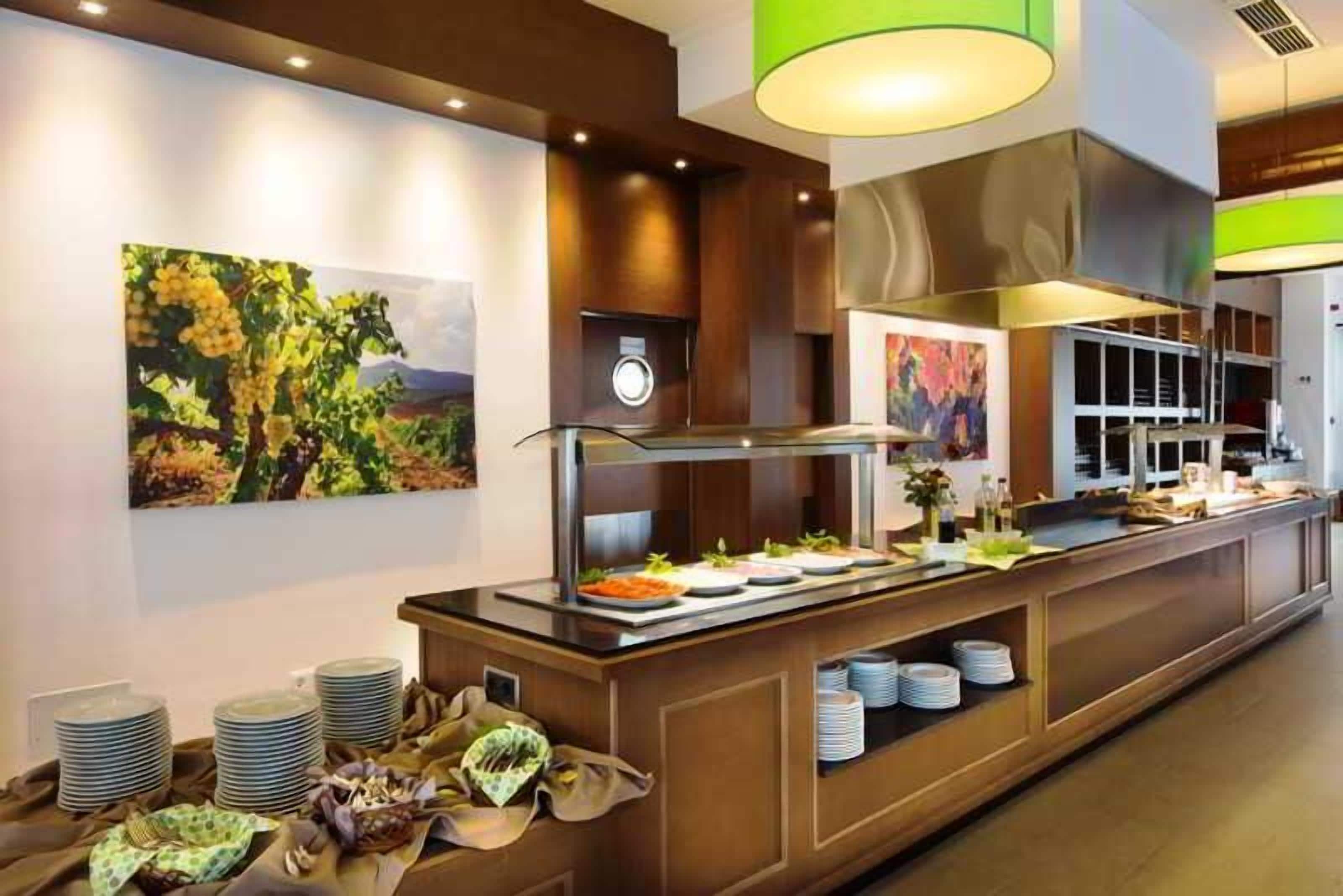 Un área de buffet con una estación de servicio central, un cuadro grande en la pared y una cocina moderna al fondo.