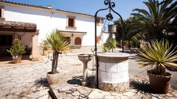 A courtyard with a stone fountain, potted plants, and a white building with a tiled roof. - Sa Bassa Plana (Llucmajor)