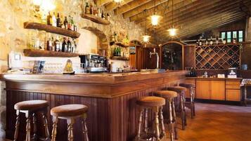 A bar area with wooden bar stools, shelves with bottles, and a rustic stone wall.