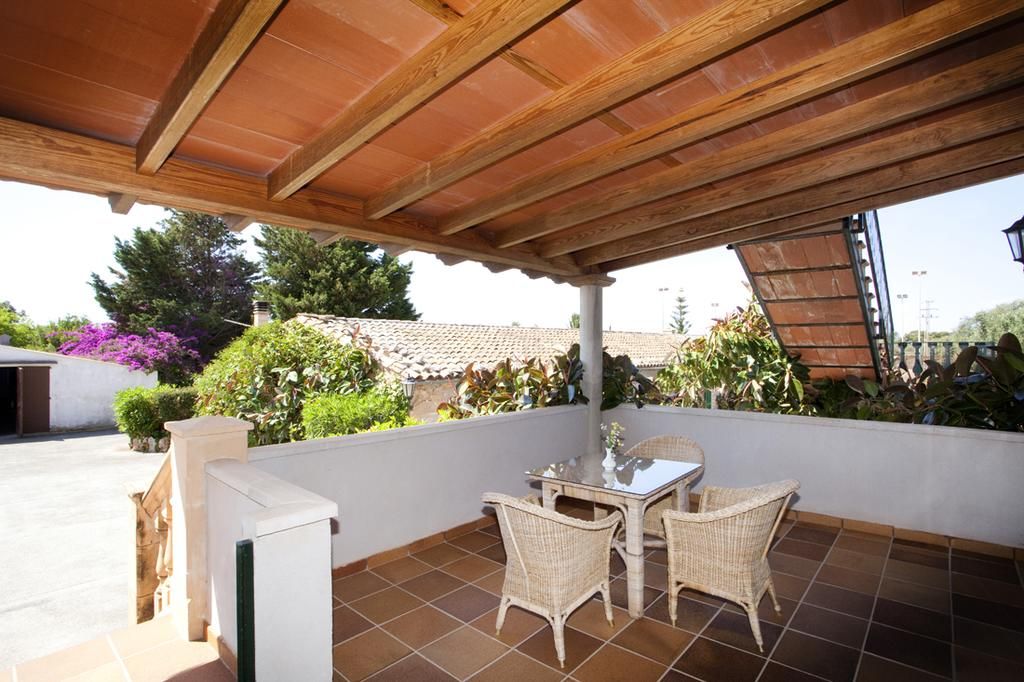 Un patio cubierto con mesa y sillas, rodeado de vegetación y un piso de baldosas.