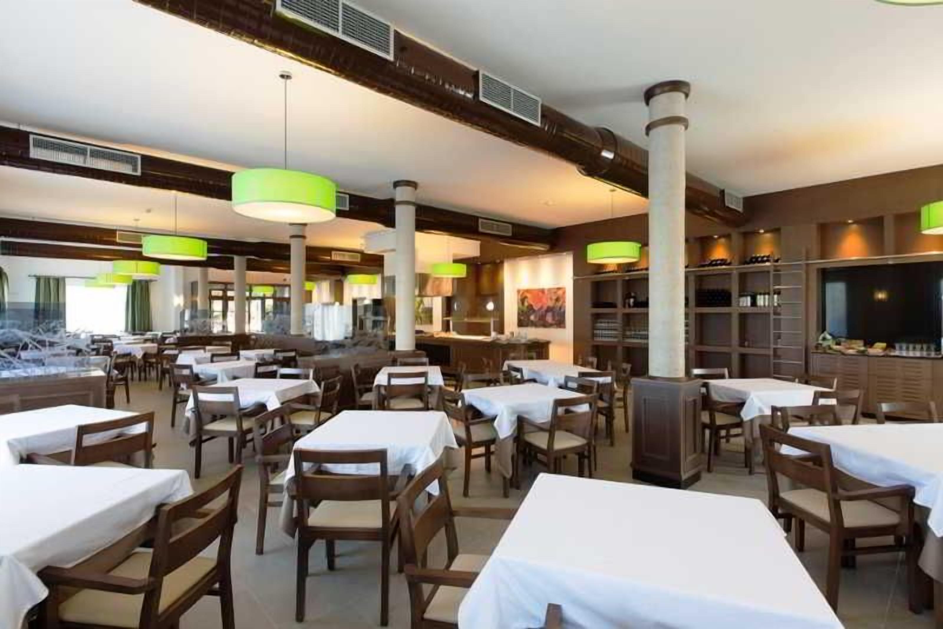 Un restaurante con varias mesas y sillas, una zona de bar y una pantalla grande.