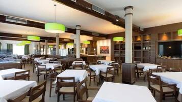Un restaurante con varias mesas y sillas, una zona de bar y una pantalla grande.