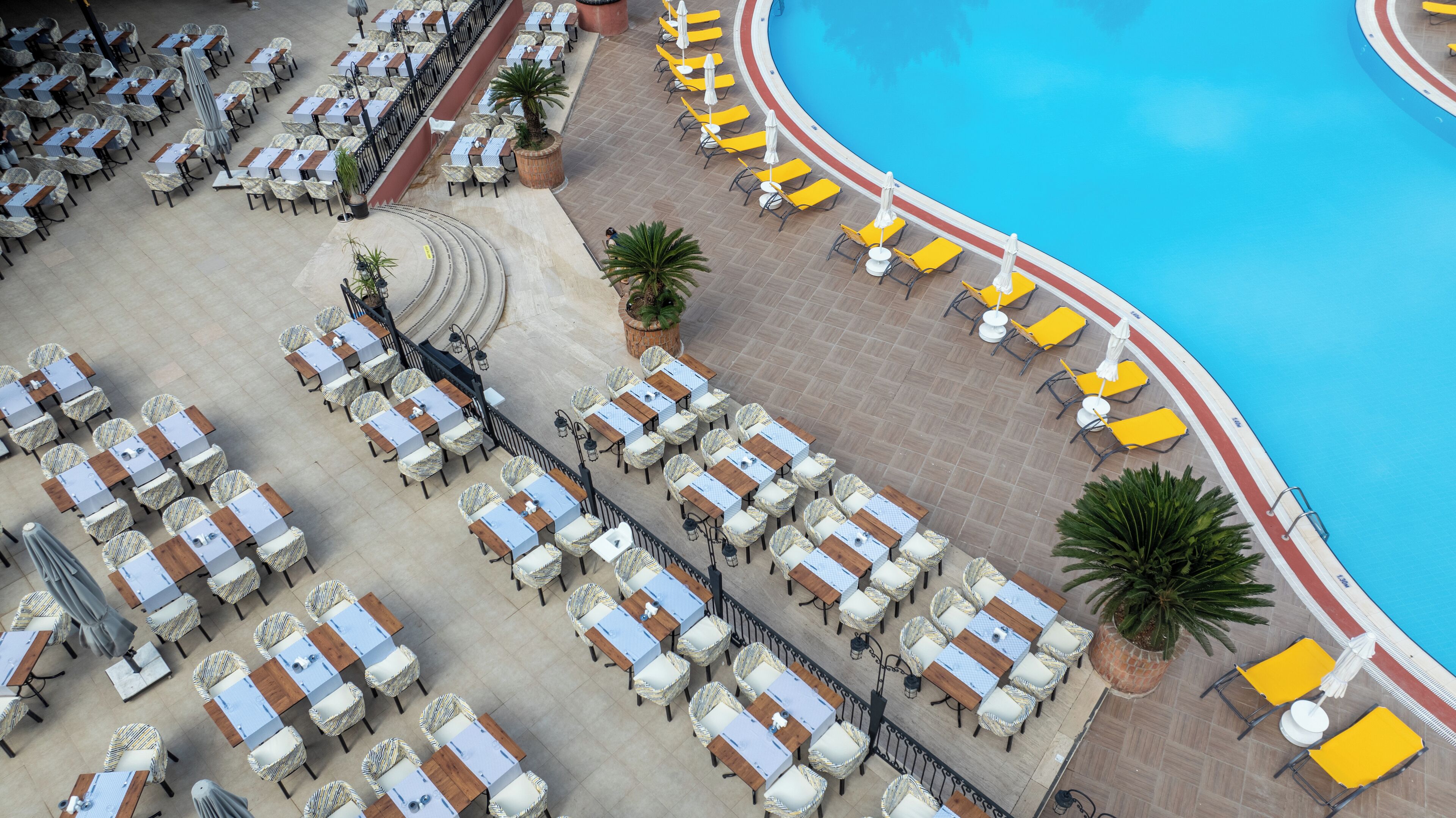 An outdoor pool area with multiple seating arrangements, including tables and chairs, and a poolside walkway.