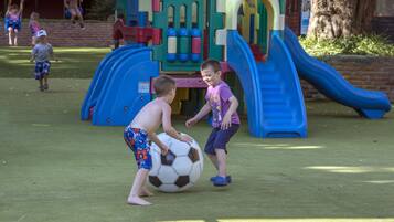 Des enfants jouent au ballon dans un parc avec des toboggans et des structures d’escalade.