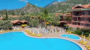 A resort with a large pool surrounded by sun loungers and umbrellas, a bar area, and buildings with red-tiled roofs. - Sundia By Liberty Suncity - All inclusive (Fethiye)