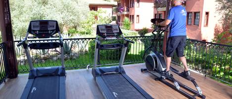 A covered outdoor area with two treadmills and a stationary bike.