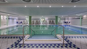 A large indoor swimming pool with clear water, surrounded by lounge chairs and a tiled floor with a checkered pattern. - Aquamarin Hotel & Spa (Kuehlungsborn)