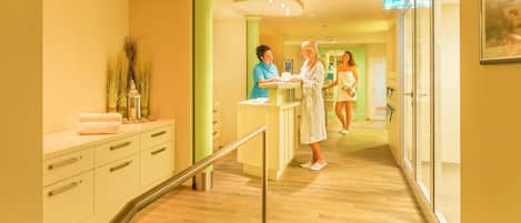 Zona de recepción de un hotel, con mostrador, área de espera y un pasillo que conduce a otras habitaciones.
