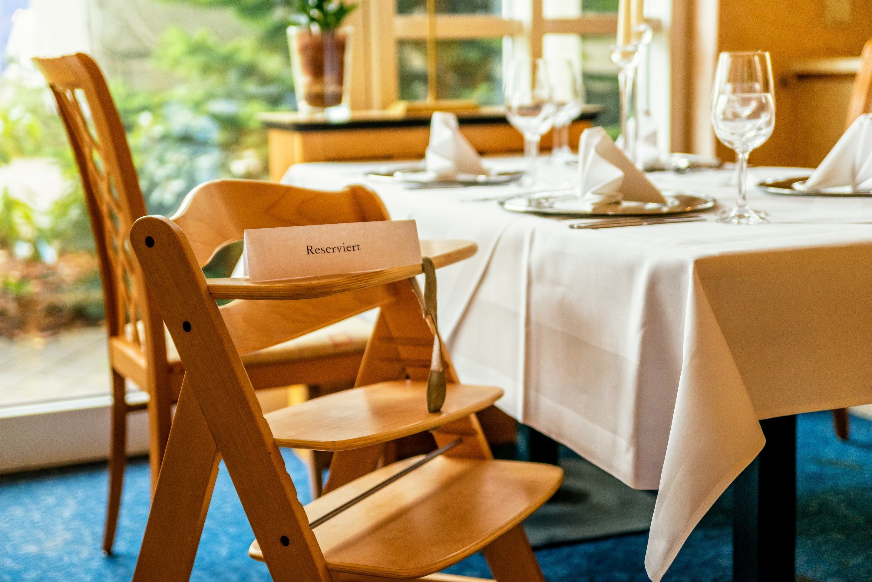A dining table set with white tablecloths, wooden chairs, and a name card holder.