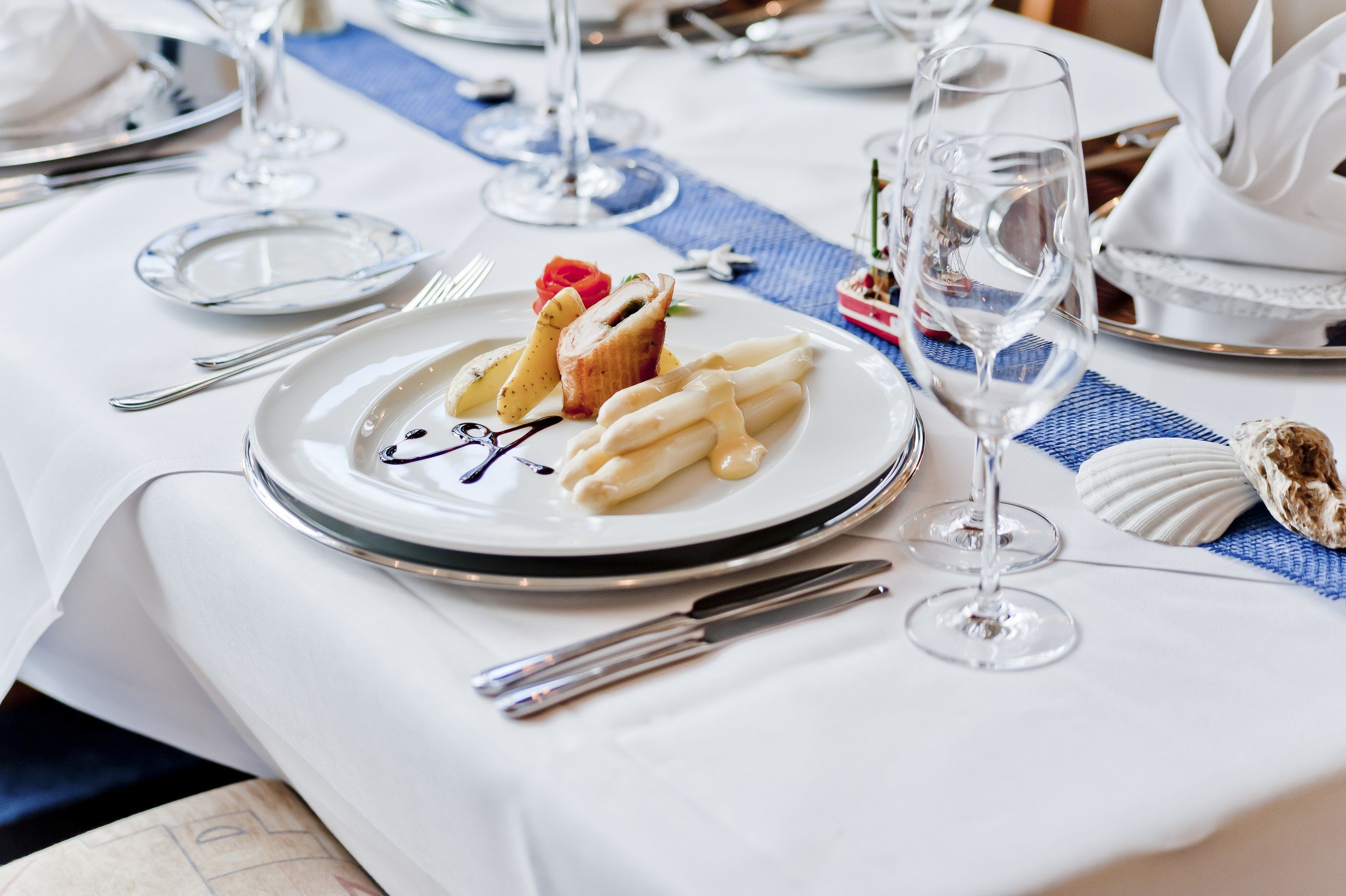 Ein Tisch, gedeckt mit weißen Tellern, Besteck und Weingläsern, mit einer Nachspeise, verziert mit einer Rose und Schokoladenglasur.