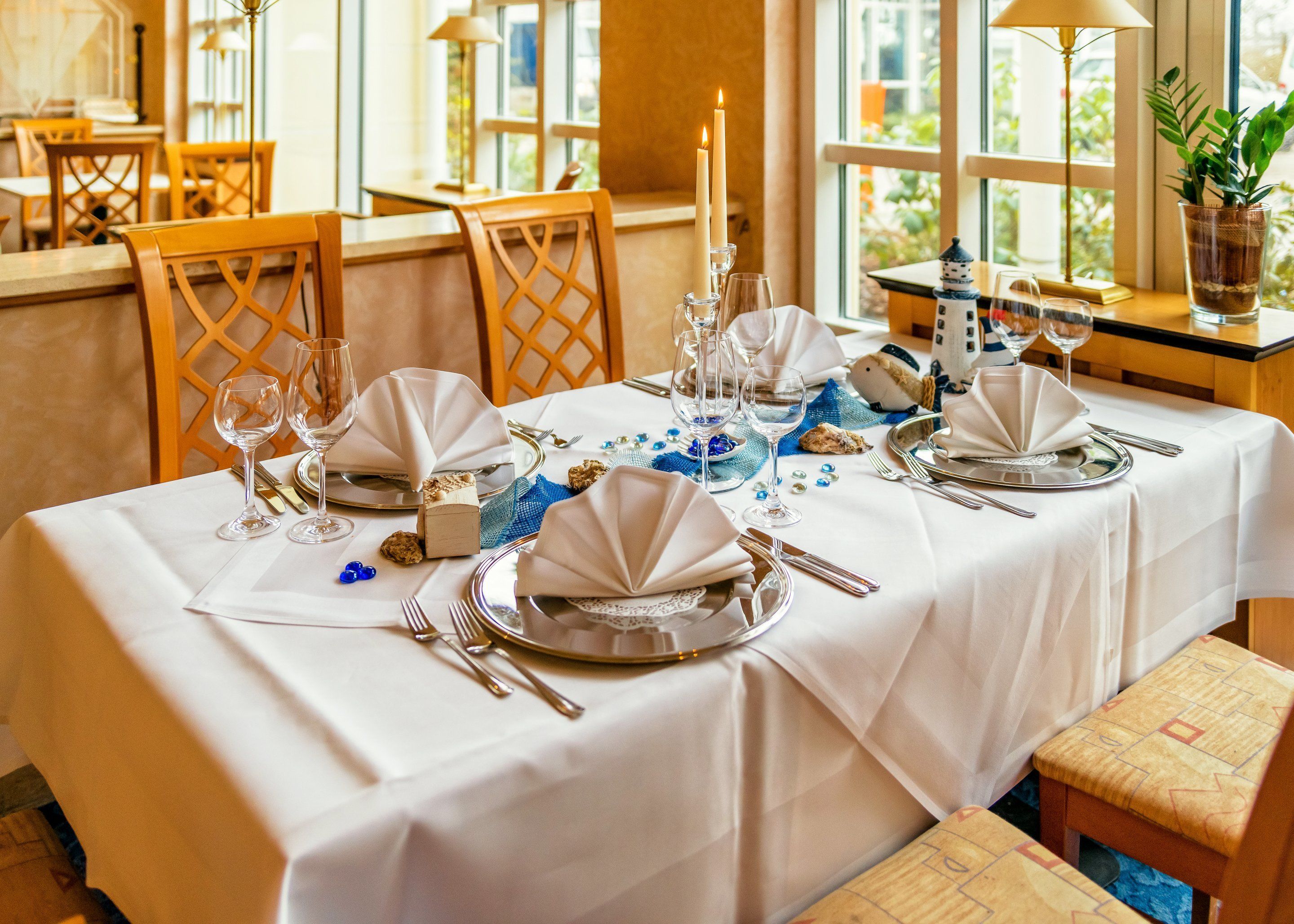 A dining table set for a meal with white tablecloths, silverware, and blue decorative elements.