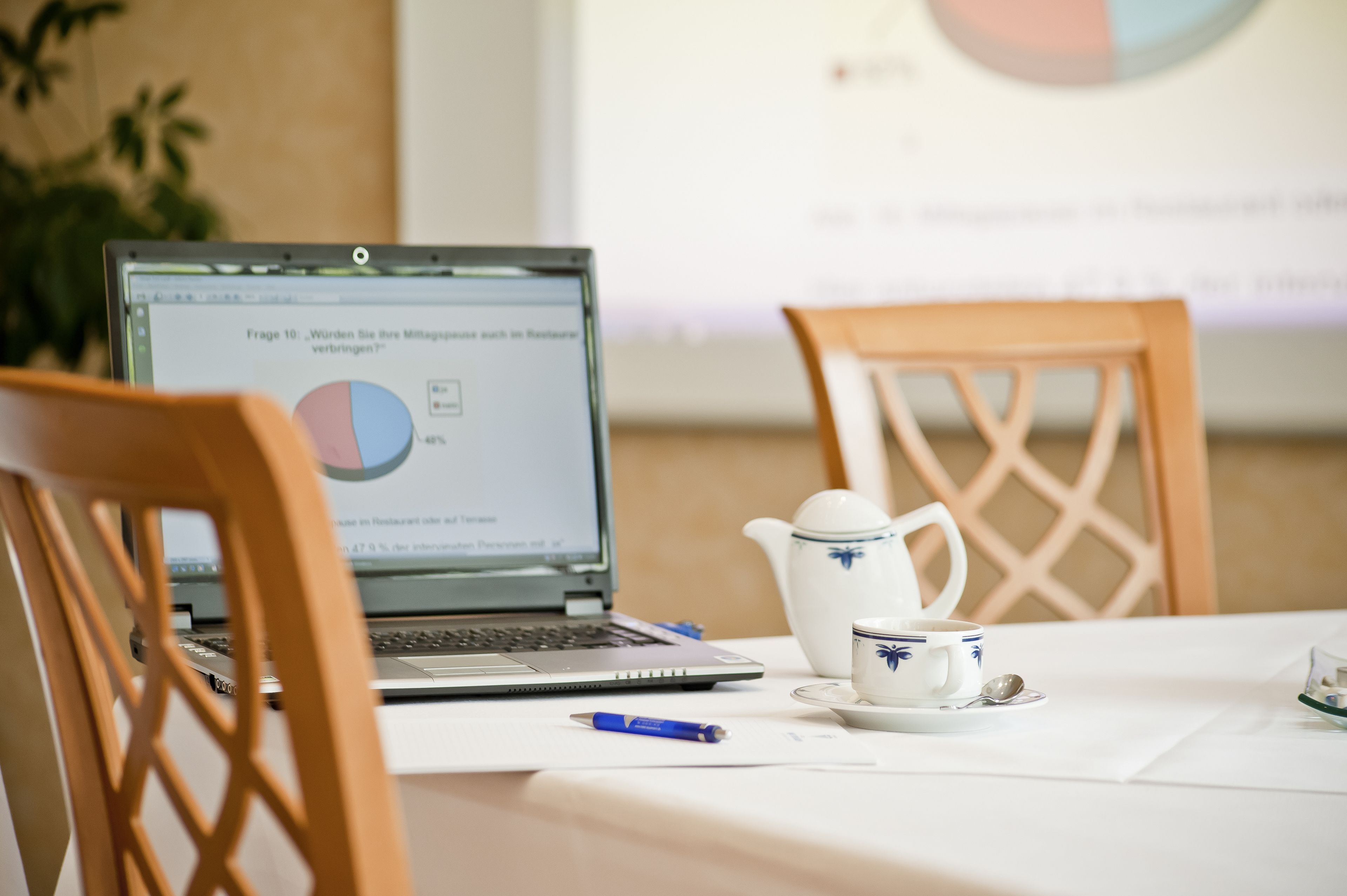 Ein Laptop auf einem Tisch mit einem Kreisdiagramm auf dem Bildschirm, eine Teekanne, eine Tasse und ein Löffel.