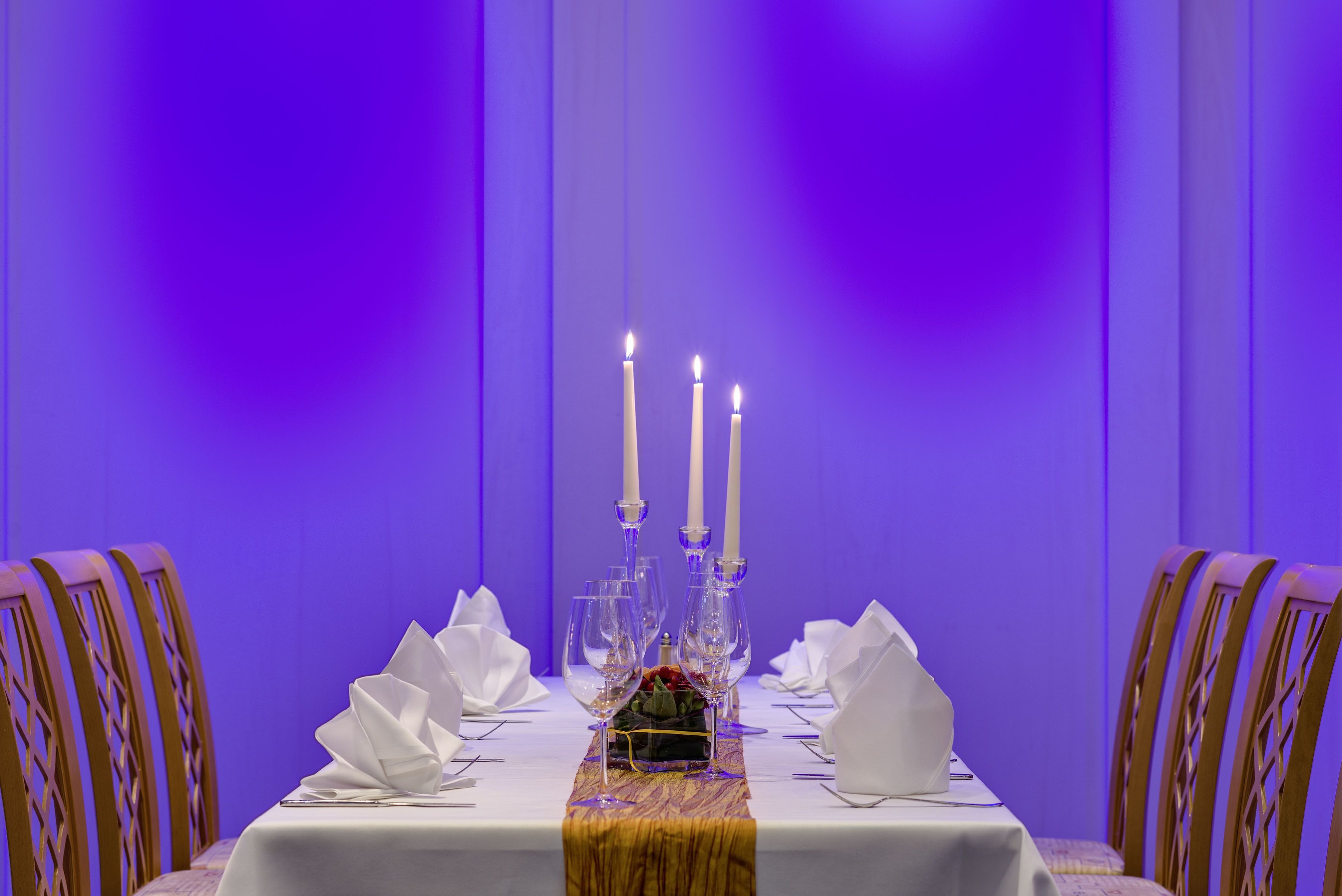 A dining table set with white napkins, wine glasses, and three lit candles.