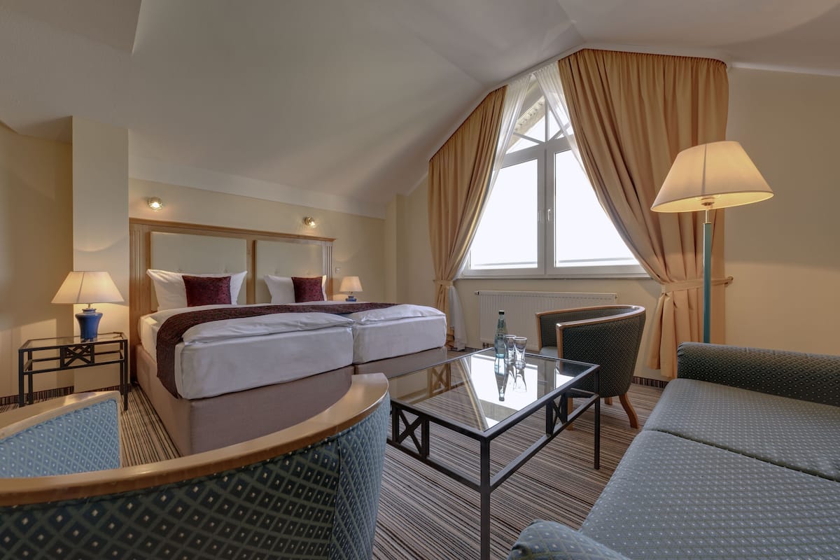 A hotel room with a bed, two bedside tables with lamps, a glass coffee table, a sofa, and a chair.
